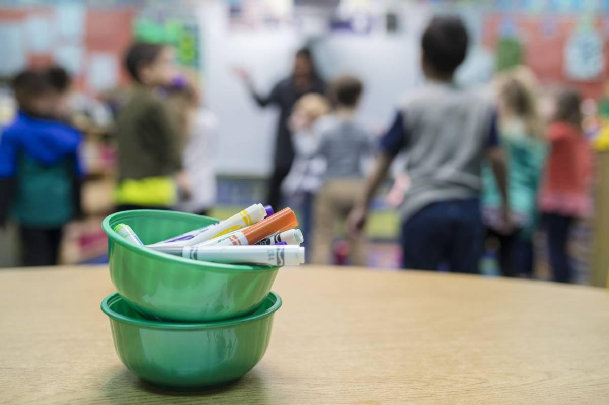 Teacher working with a group of students behind a bowl of markers on a table.